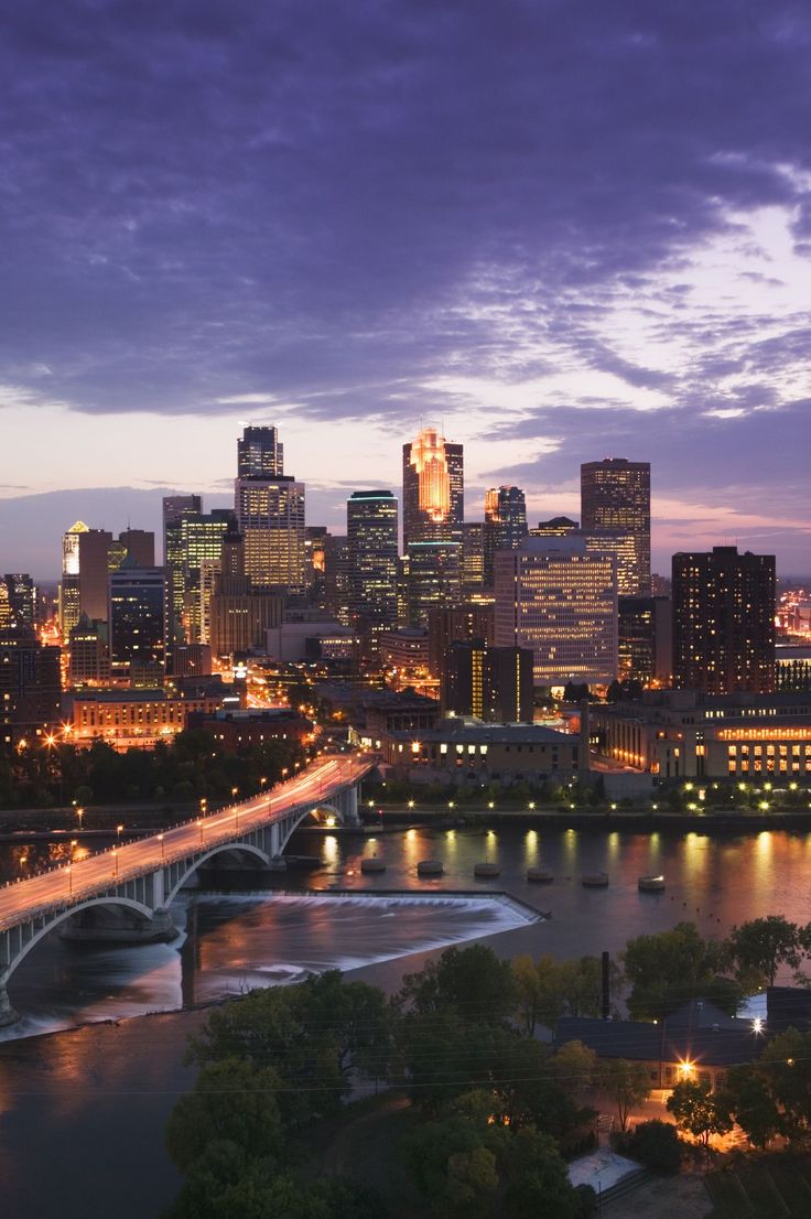 the city skyline is lit up at night, with lights on and bridge in foreground