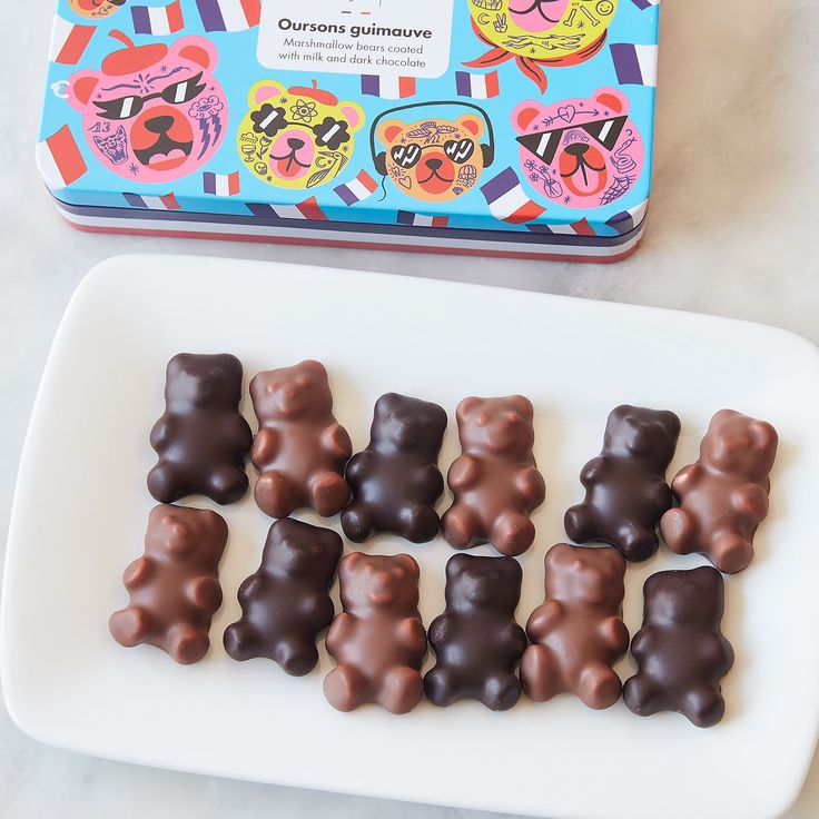 chocolate candies in the shape of bears on a plate next to a tin of candy