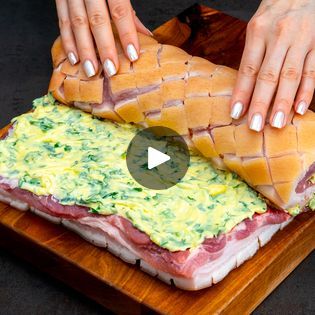 a woman is cutting into a large sandwich on a wooden platter with cheese and other toppings