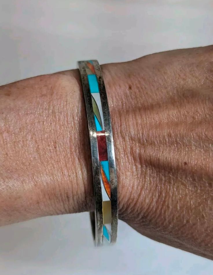 This vintage Zuni bangle bracelet is a true work of art, crafted from sterling silver and inlaid with multiple colorful stones. The round shape and slide closure make it easy to wear, perfect for occasions like Mother's Day, Christmas, graduation, birthdays, and even Valentine's Day. Handmade by Native American artisans, this bracelet showcases the beauty and ethnic style of the Zuni tribe. The multi-stone inlay features many different shapes and colors, including turquoise and other unknown treatments. The bracelet is 7 inches long and stackable, with a signed signature that adds to its authenticity and uniqueness.  Signed Zuni Piece, Hard to Make out the Signature. Condition is Pre-owned. Please Refer to Pictures for Condition Details and Measurements. Multicolor Bangle Bracelets For Anniversary, Multicolor Round Collectible Jewelry, Multicolor Round Jewelry With Polished Finish, Multicolor Polished Round Jewelry, Multicolor Inlay Sterling Silver Bracelets, Multicolor Sterling Silver Bracelets With Inlay, Multicolor Sterling Silver Bracelet With Inlay, Sterling Silver Collectible Bangle, Artisan Bangle Bracelets With Inlay