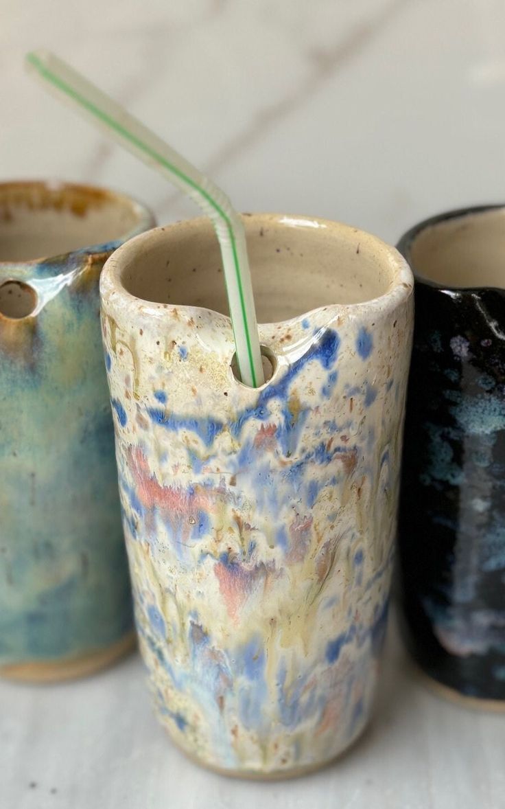 three cups with straws in them sitting on a table next to each other and one cup has a straw sticking out of it