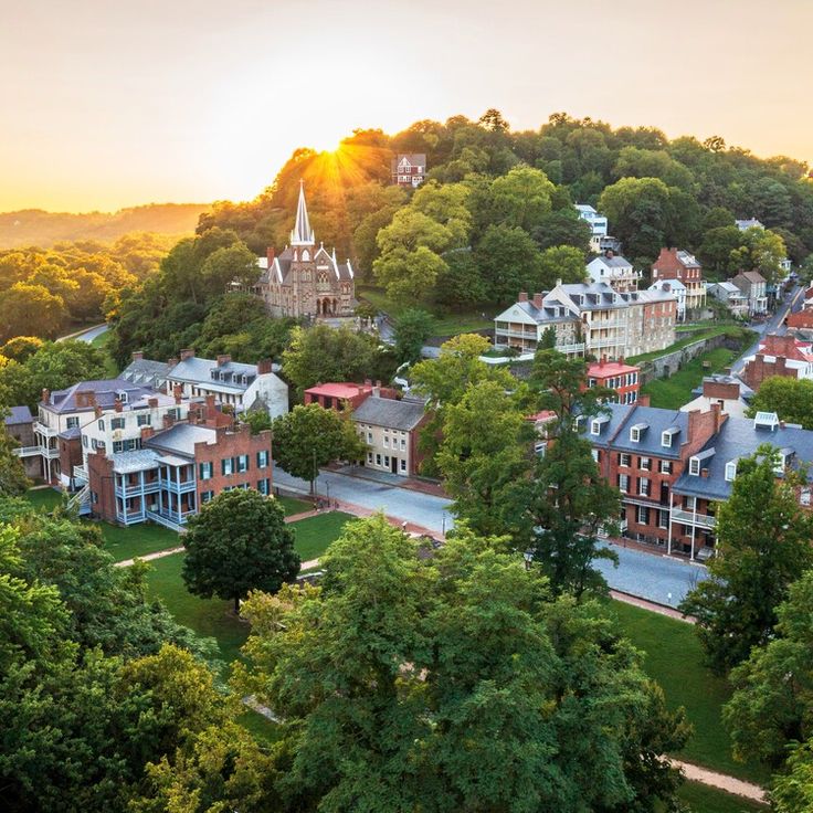 an aerial view of a town surrounded by trees and buildings with the sun setting in the background