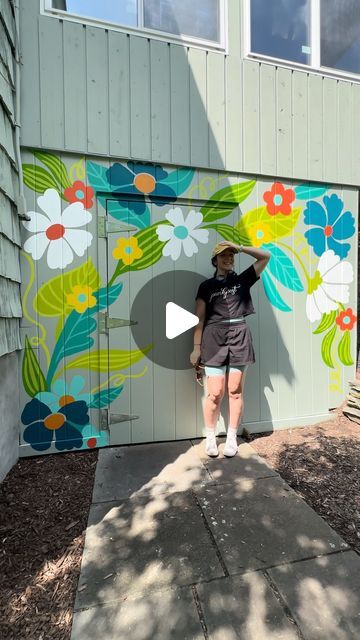 a woman is standing in front of a painted garage door with flowers on the side