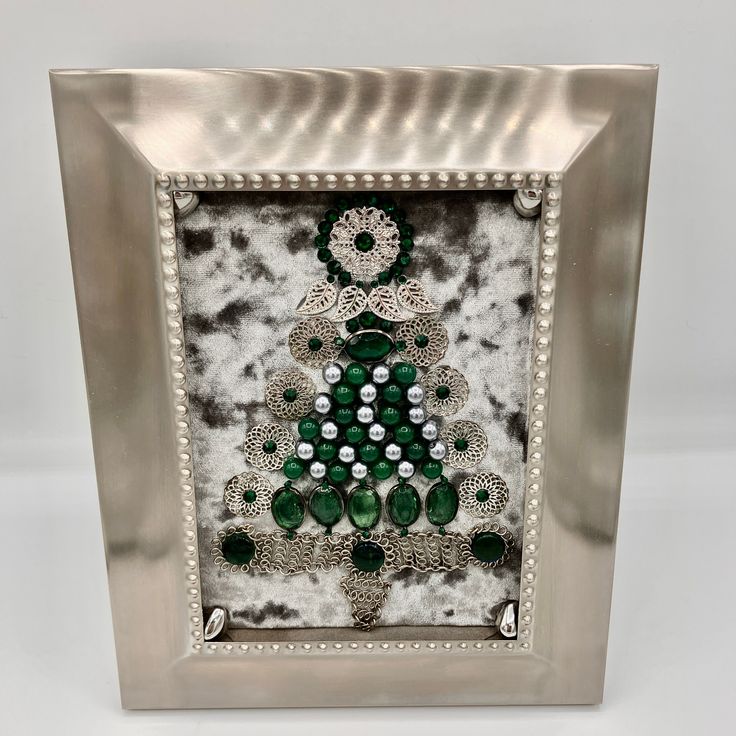 Framed vintage jewelry in silver and emerald green Christmas tree theme. Made with vintage chain choker necklace with emerald green glass beads, silver tone filigree earring pieces, faux silver pearls, glass emerald green beads, silver-tone leaves, green rhinestones and glass emerald green beads. Argento sc polished metal frame with inset configuration. Easel back frame. Approximately 8 x 10 inches. Elegant Christmas Celebration Jewelry, Nickel-free Jewelry For Festive Holiday, Nickel-free Jewelry For Festive Holidays, Holiday Festive Nickel-free Jewelry, Holiday Party Silver Necklaces, Holiday Party Silver Necklace, Beaded Emerald Jewelry Gift, Decorative Metal Jewelry Gift, Elegant Silver Holiday Jewelry