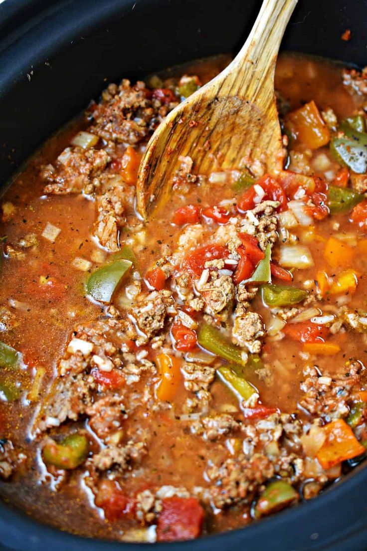 a wooden spoon in a slow cooker filled with chili and ground beef soup, ready to be eaten