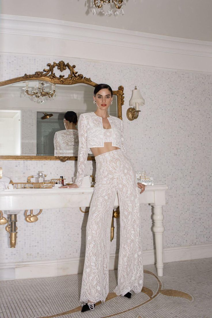 a woman standing in front of a bathroom sink wearing white pants and a crop top