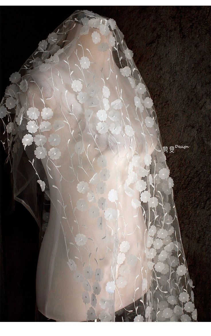 a white veil with flowers on it is shown in front of a mannequin