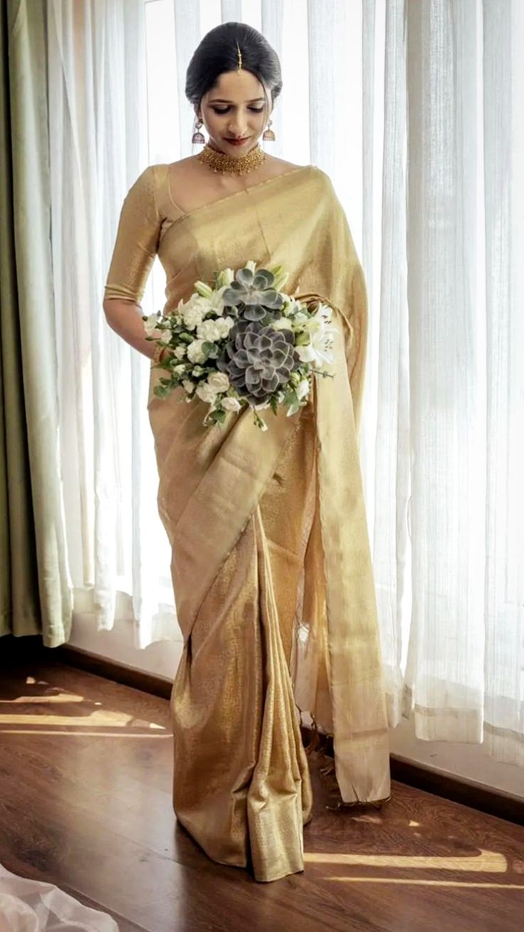 a woman standing in front of a window wearing a gold sari with flowers on it