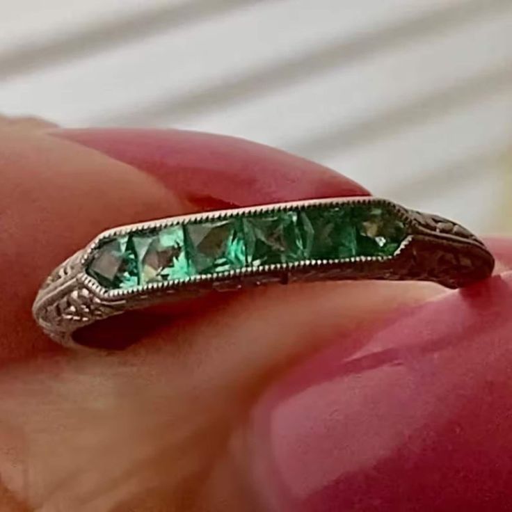 a close up of a person's hand holding a ring with green stones on it