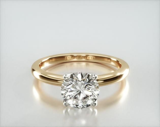 a yellow gold engagement ring with a round cut diamond in the center, on a white background