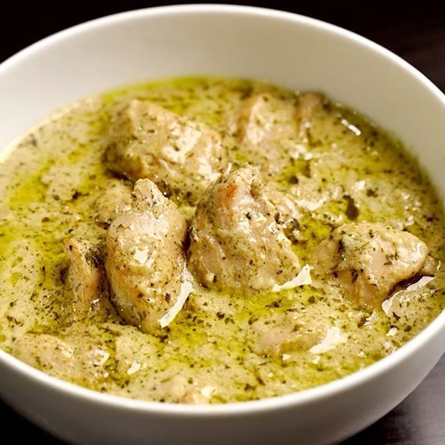 a white bowl filled with chicken and pesto soup on top of a wooden table