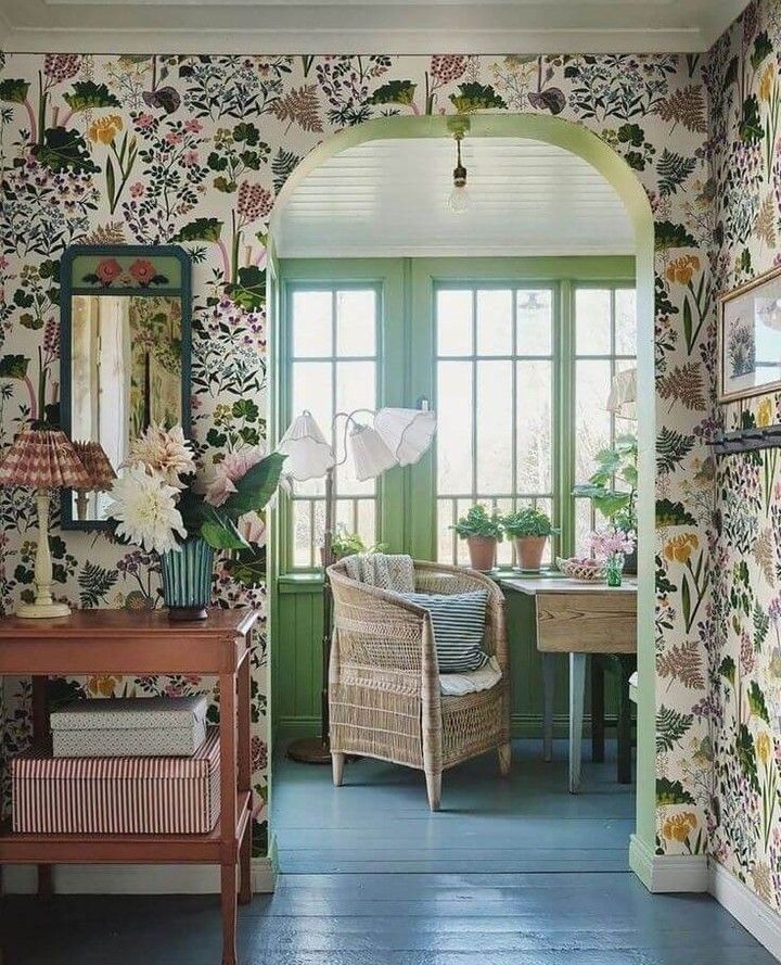 a living room with floral wallpaper and green trim on the walls, along with a wicker chair