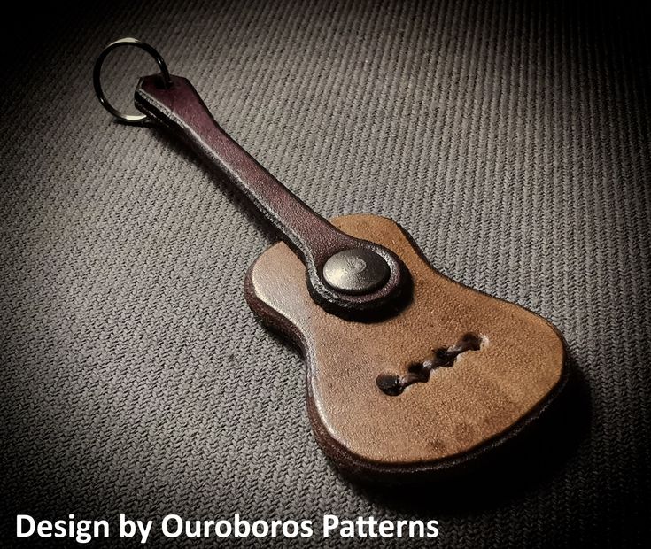 a wooden guitar keychain sitting on top of a gray surface with the words design by outdoorss patterns