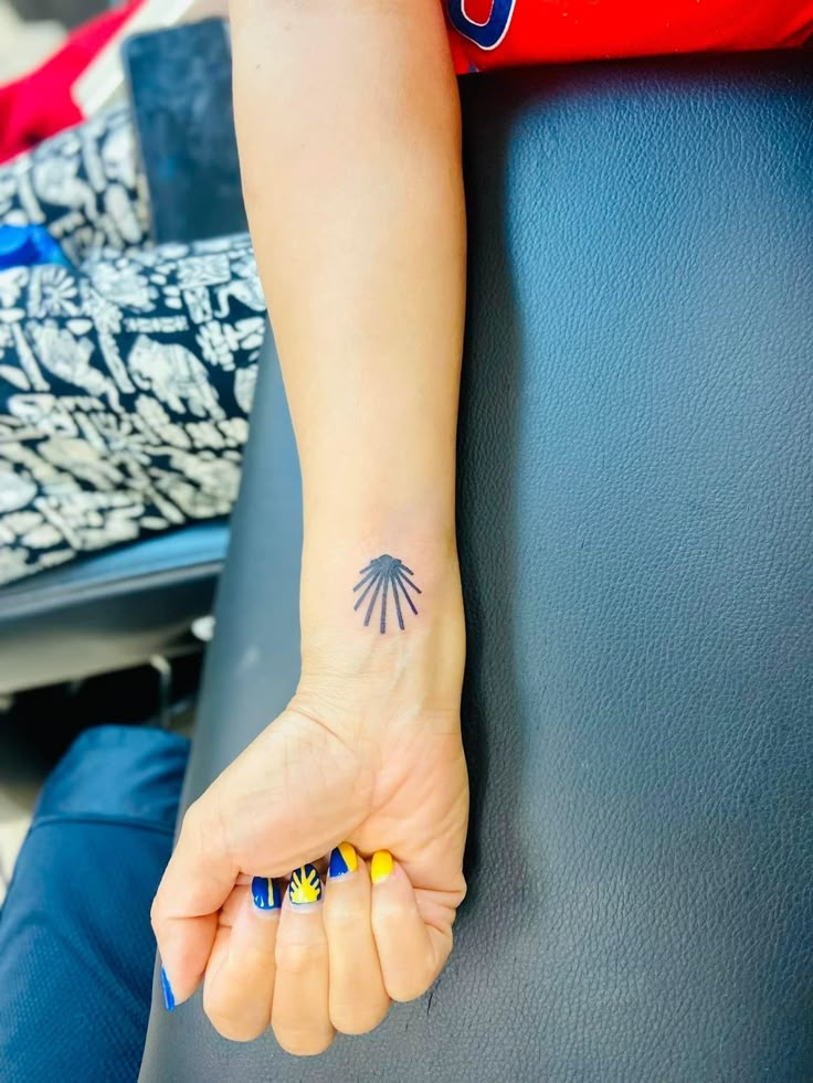 a small palm tree tattoo on the left wrist and right hand with yellow, blue, and black nails