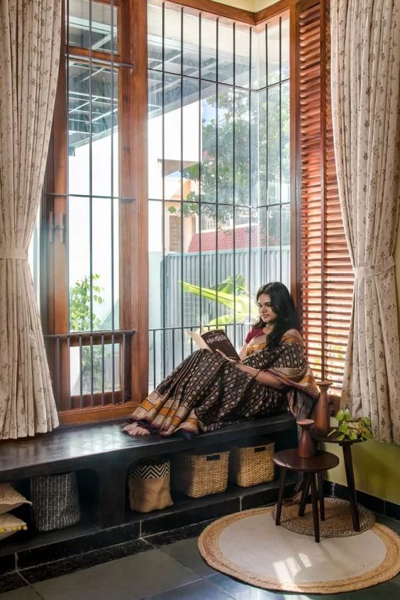 a woman sitting on a window sill reading a book in front of a large window