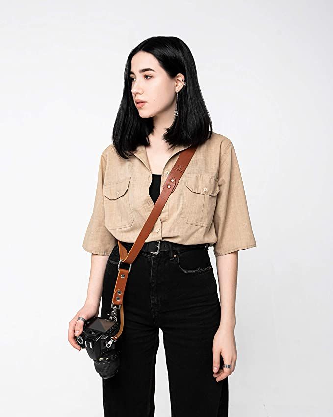 a woman holding a camera in her right hand and wearing a brown shirt with short sleeves