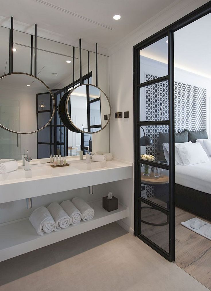 a white bathroom with two mirrors and towels on the counter, next to a bed