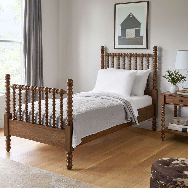 a wooden bed with white sheets and pillows in a room next to a lamp on a table