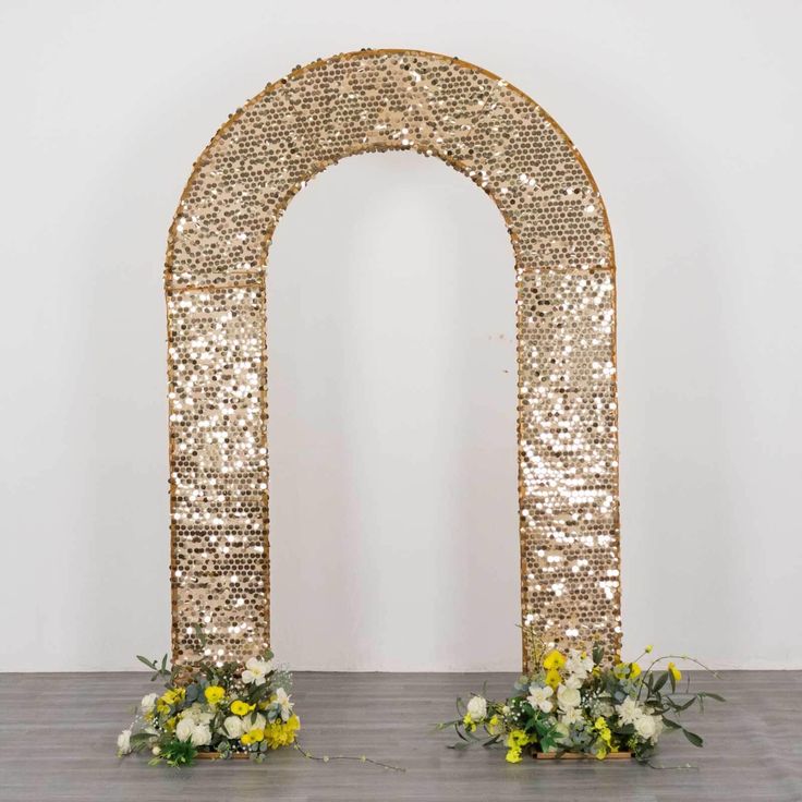 an arch made out of gold sequins with flowers on the floor in front