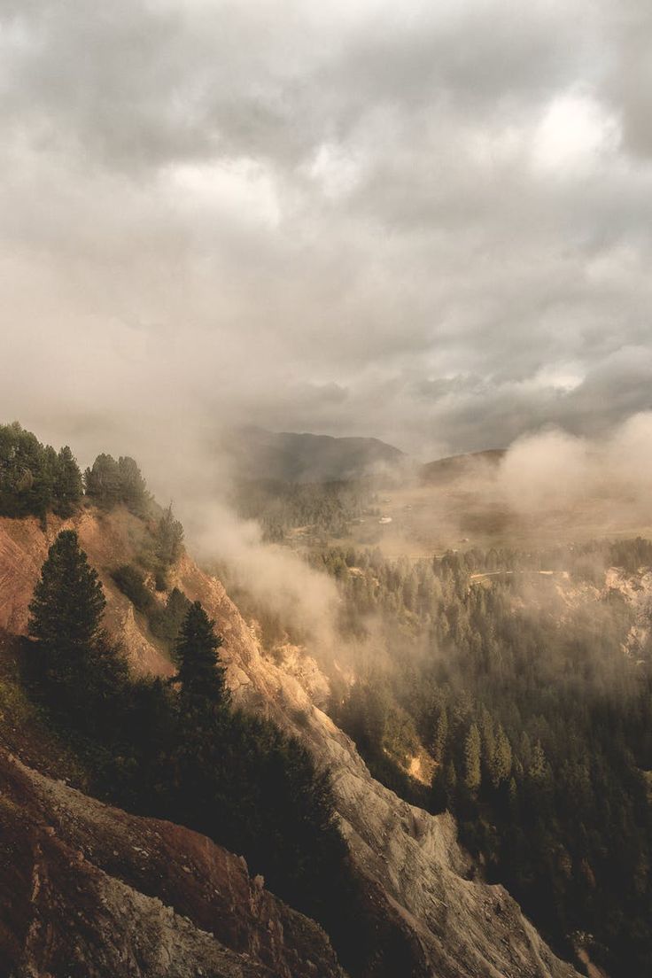 the mountains are covered in fog and clouds as seen from an overlook point on a cloudy day