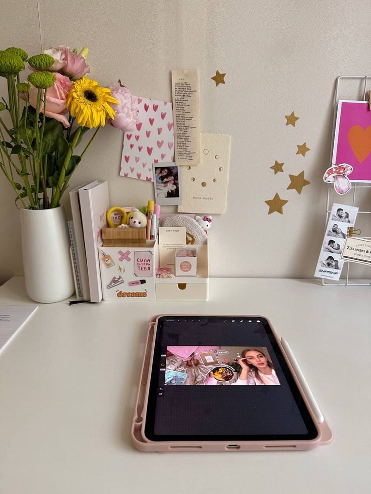 a tablet computer sitting on top of a desk next to a vase filled with flowers