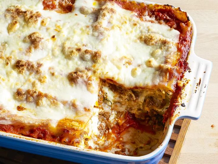 a casserole dish with meat, cheese and sauce in it on a wooden table