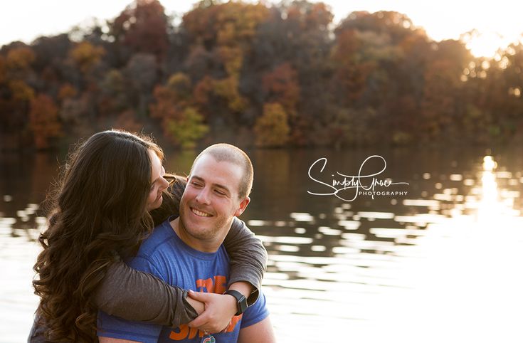 a man and woman hugging each other in front of a body of water with trees in the background