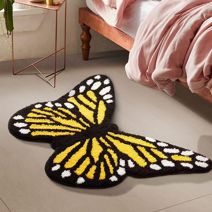 a yellow and black butterfly rug sitting on the floor next to a bed with pink sheets