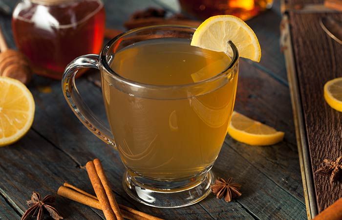 a glass mug filled with liquid surrounded by cinnamons and honey