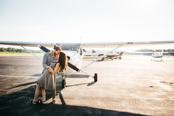 a couple kissing in front of an airplane on the tarmac with another plane behind them