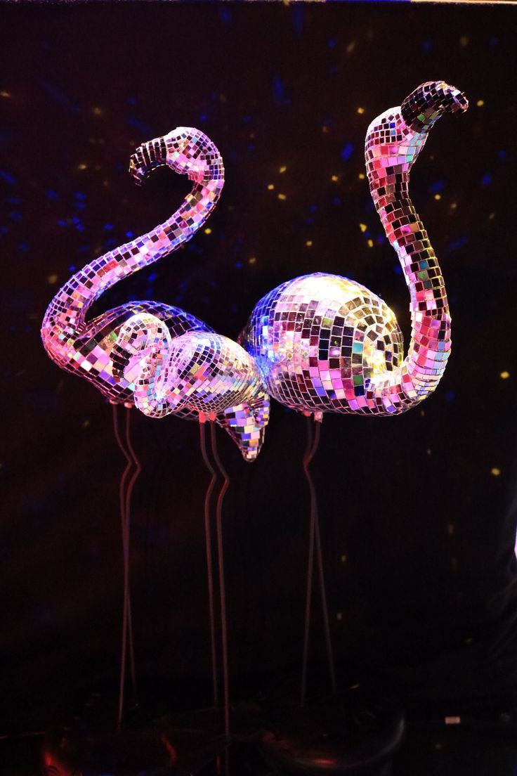 two flamingos made out of disco - tiles are standing in front of a black background