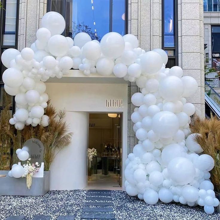 an arch made out of white balloons in front of a building with plants and potted grass