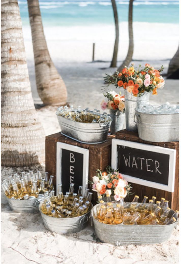 there are many bottles and buckets on the beach with flowers in them, along with wine glasses