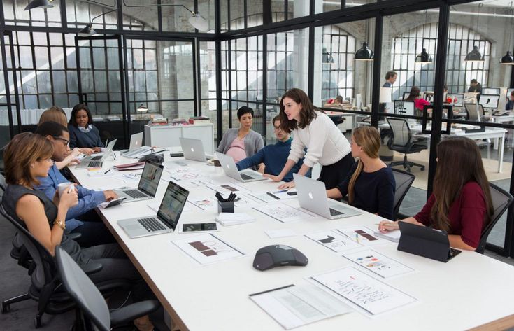 a group of people sitting around a table with laptops on it and papers in front of them