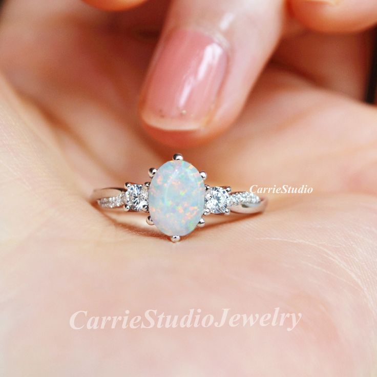 a woman's hand holding an opal and diamond ring