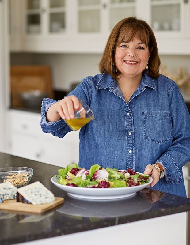 a woman pouring dressing onto a salad in a bowl