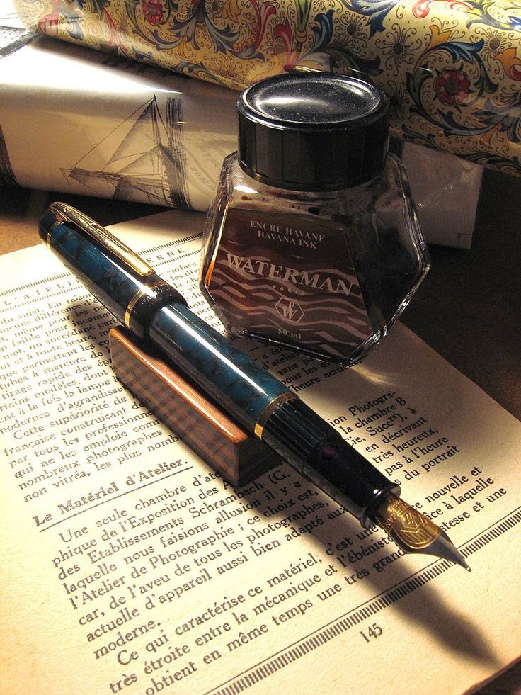 a fountain pen sitting on top of an open book next to a fountain ink bottle