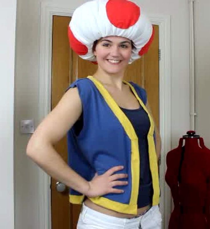 a woman standing in front of a dress up mannequin with a hat on her head