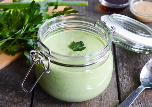 a jar filled with green liquid sitting on top of a wooden table next to spoons