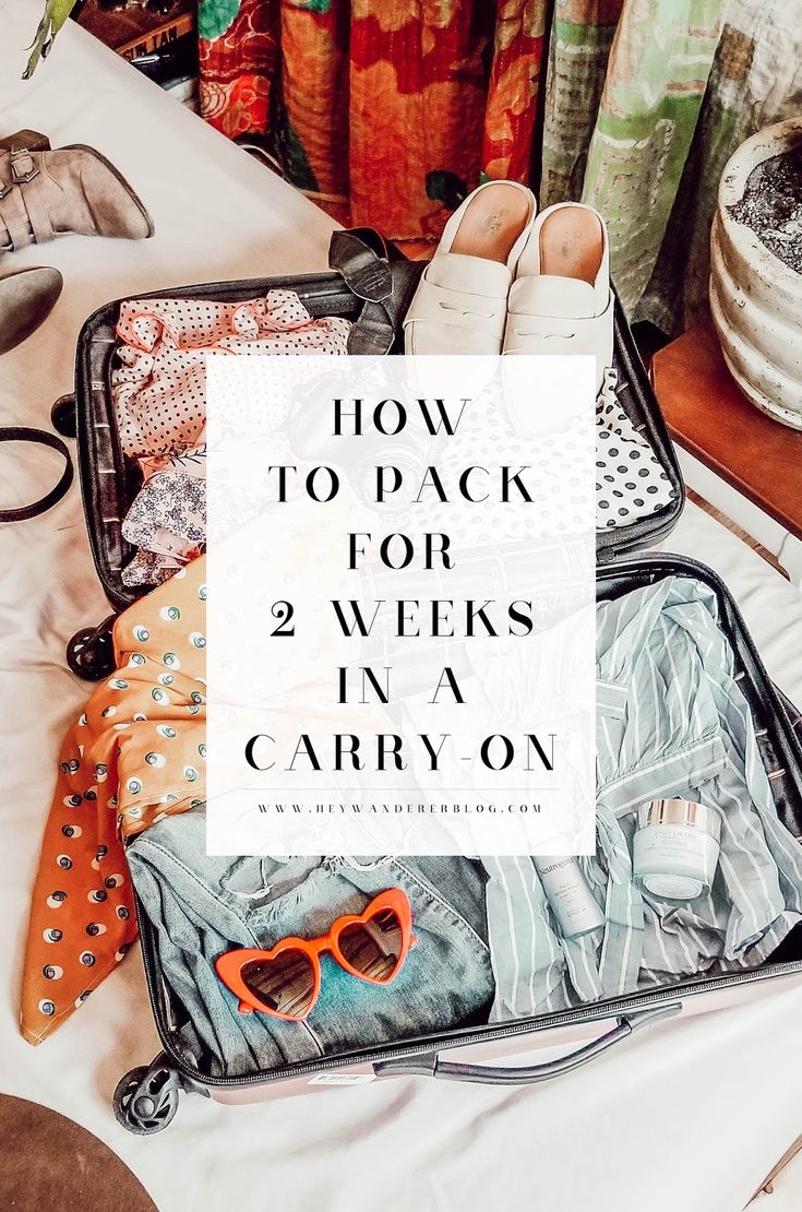 an open suitcase with clothes and sunglasses on the table next to it is text overlaying how to pack for 2 weeks in a carry on