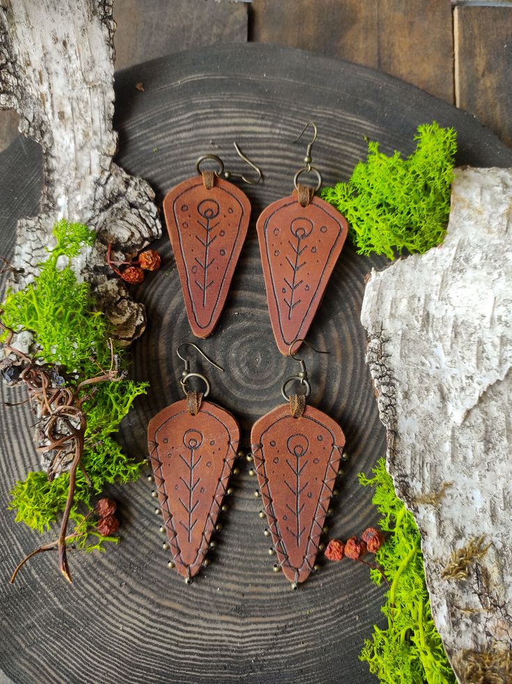 four brown leather triangle shaped earrings sitting on top of a piece of wood next to some moss