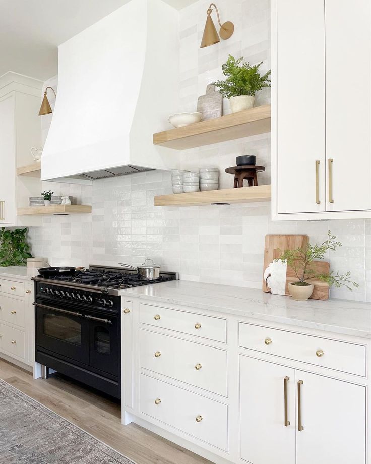 a kitchen with white cabinets and open shelves on the wall, along with a black stove top oven