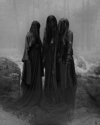 three women standing in the woods with long black hair and cloaks on their backs