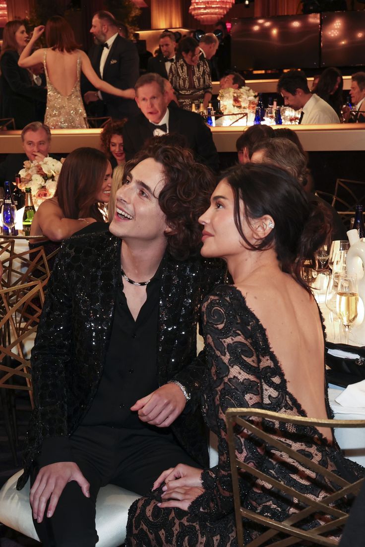 two people sitting next to each other in front of a crowd at a formal event