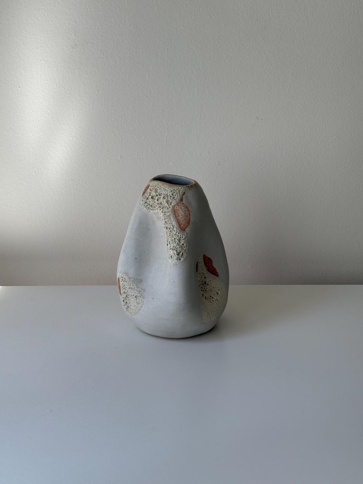 a white vase sitting on top of a table next to a wall and lamp shade