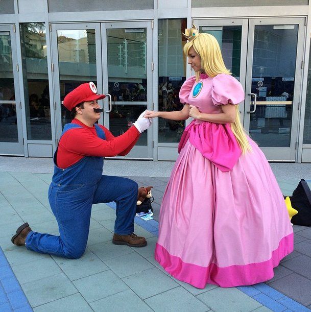 a man kneeling down next to a woman in a pink dress