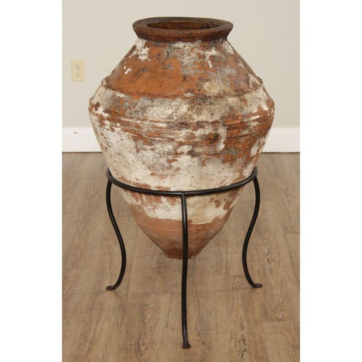 an old vase sitting on top of a metal stand with a wooden floor in the background