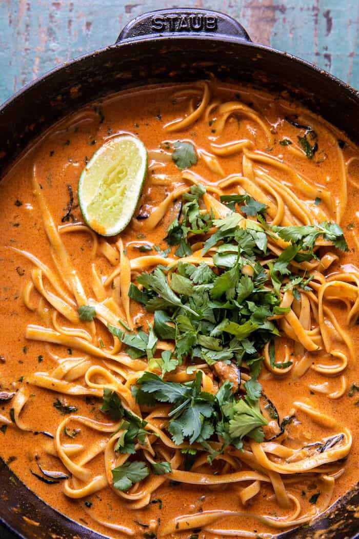 a skillet filled with pasta and garnished with cilantro, parsley and lime