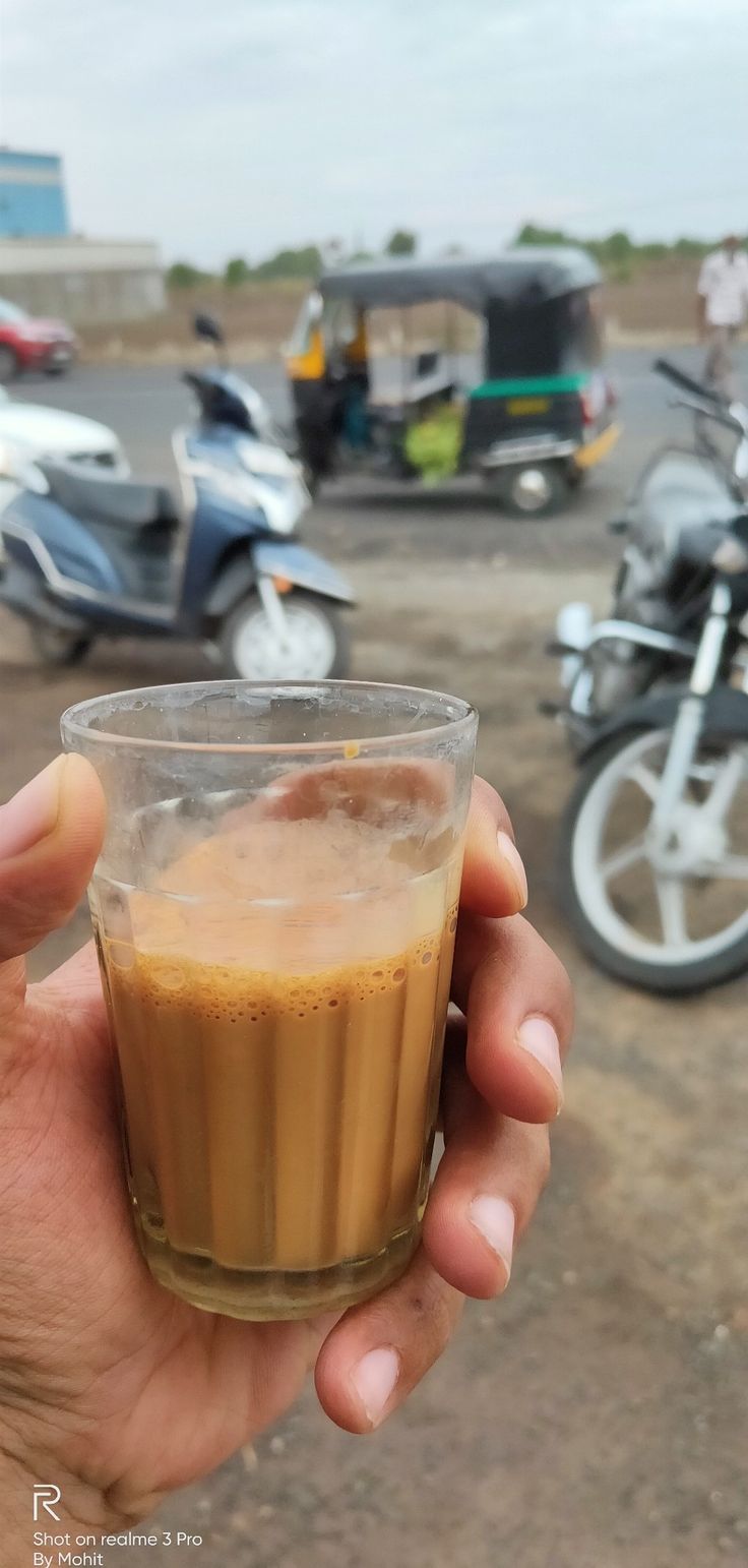 a person holding up a glass with liquid in it on the ground next to motorcycles