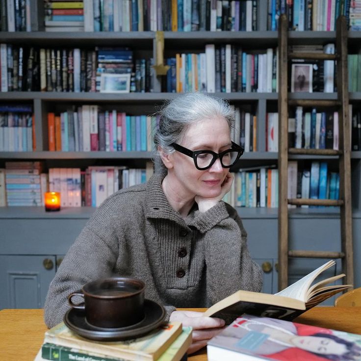 an older woman sitting at a table in front of a book shelf filled with books